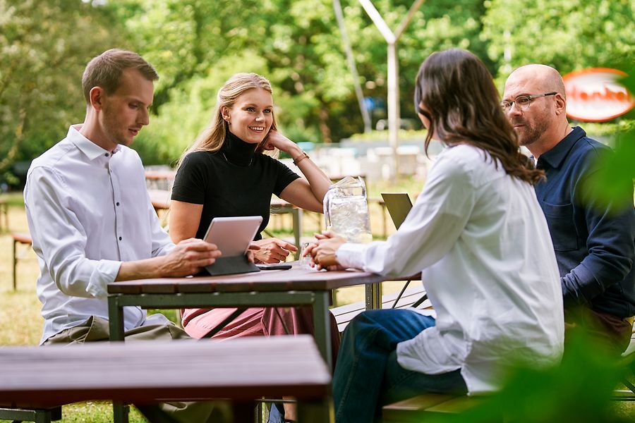 Group of colleagues sitting together outdoors, discussing work with tablets and laptops, representing collaboration and an open, team-oriented culture at Henkel.