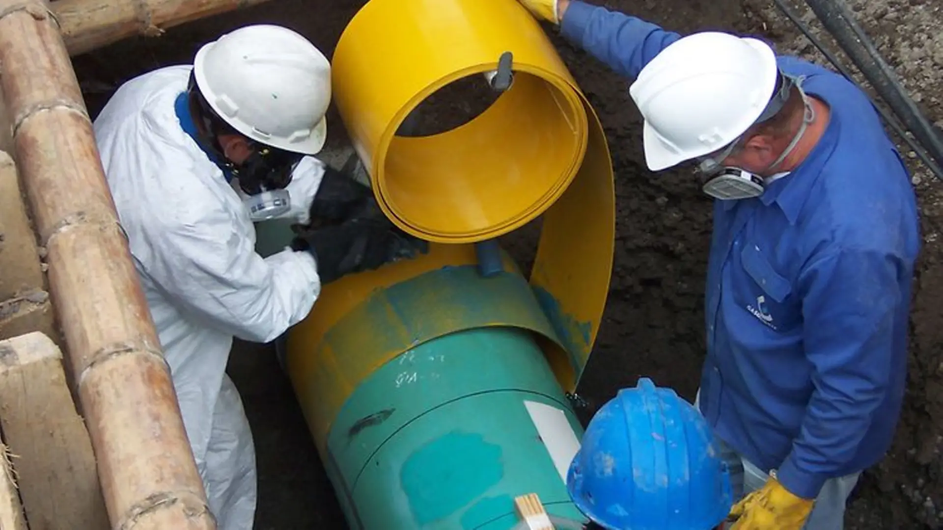Three technicians installing insulating foil on a pipe.