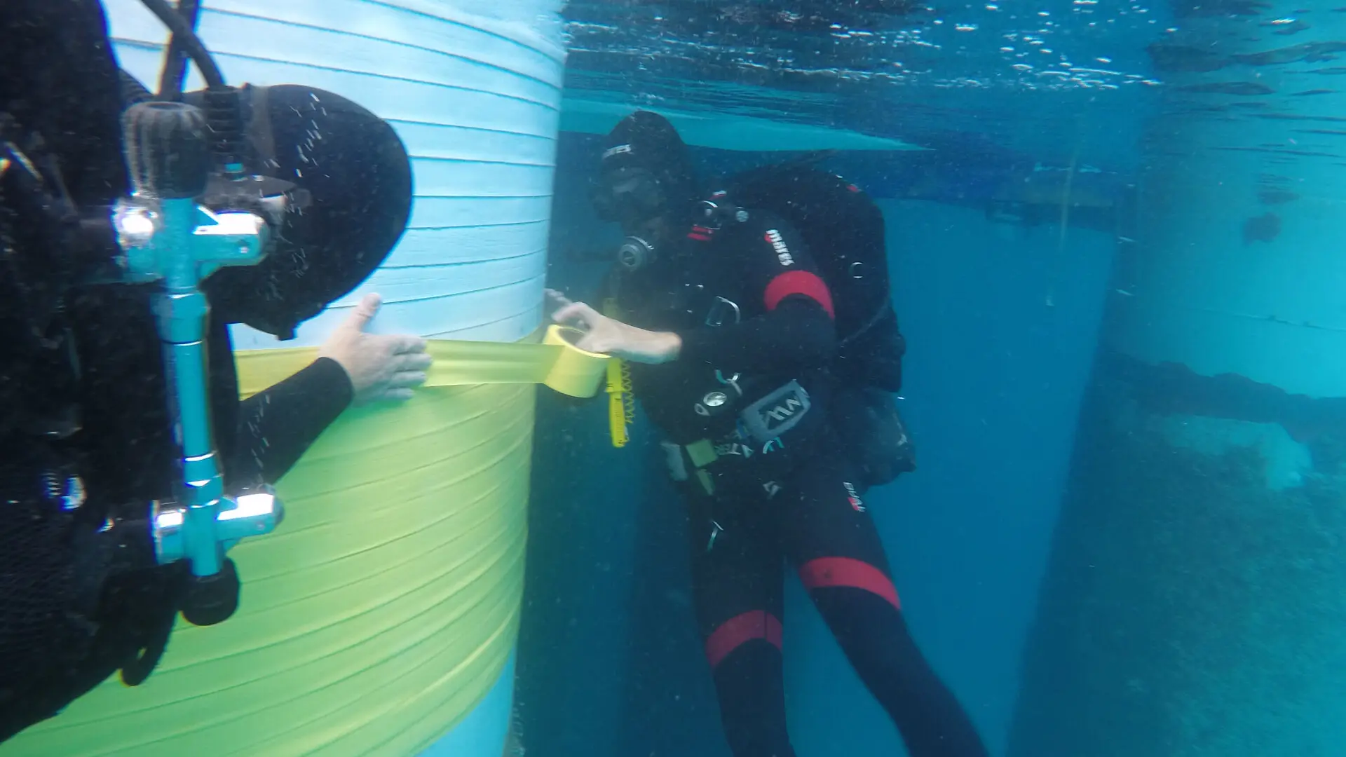 Two divers wrap an underwater pillar with a sealing film.