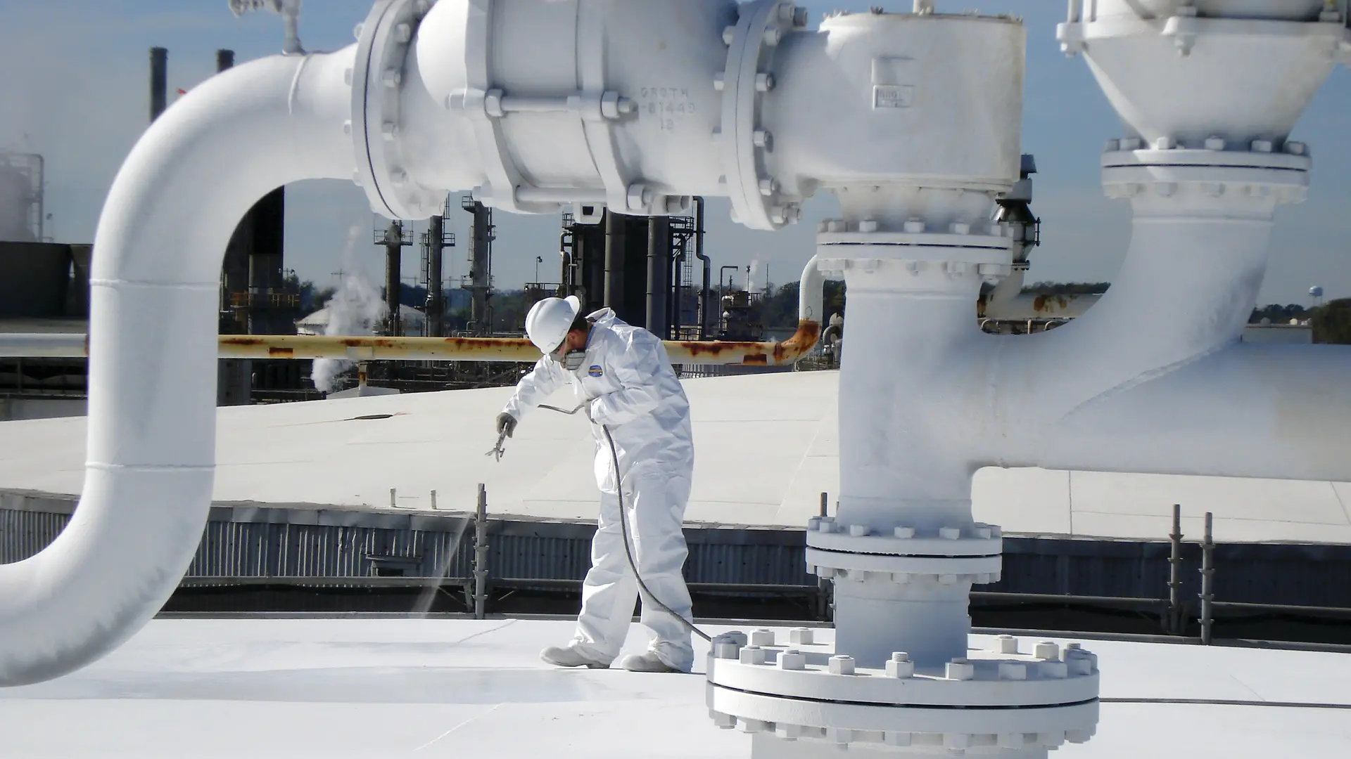 A man applies Mascoat coating on a roof in an industrial environment.