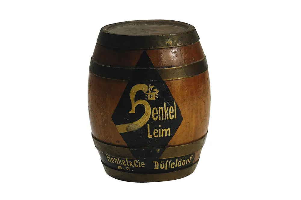 Hölzernes Fass mit der Aufschrift „Henkel Leim“ und dem alten Firmenlogo. Das Fass ist mit Metallringen eingefasst.