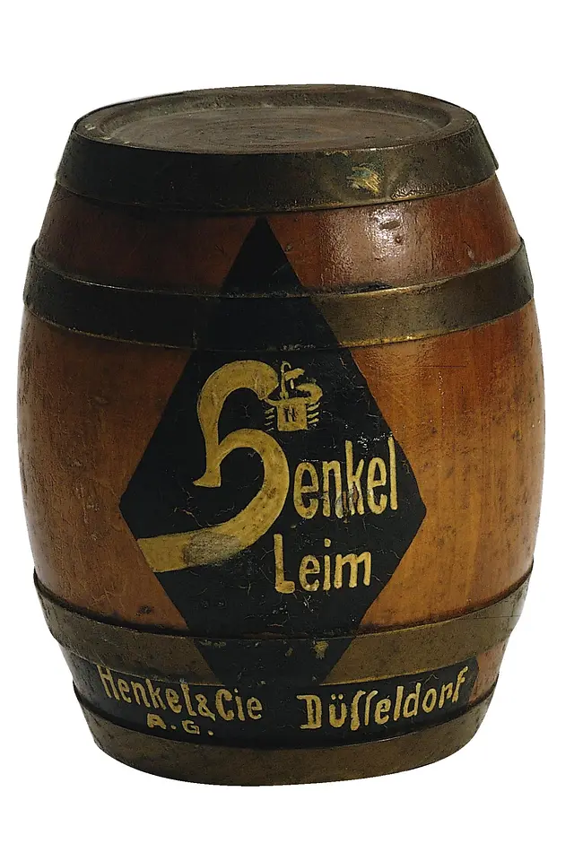Hölzernes Fass mit der Aufschrift „Henkel Leim“ und dem alten Firmenlogo. Das Fass ist mit Metallringen eingefasst.