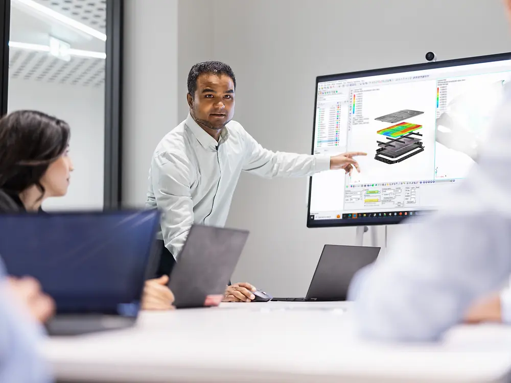 Team collaborating on innovation using Loctite solutions, with a professional presenting modeling and simulation designs on a large screen during a technical meeting.