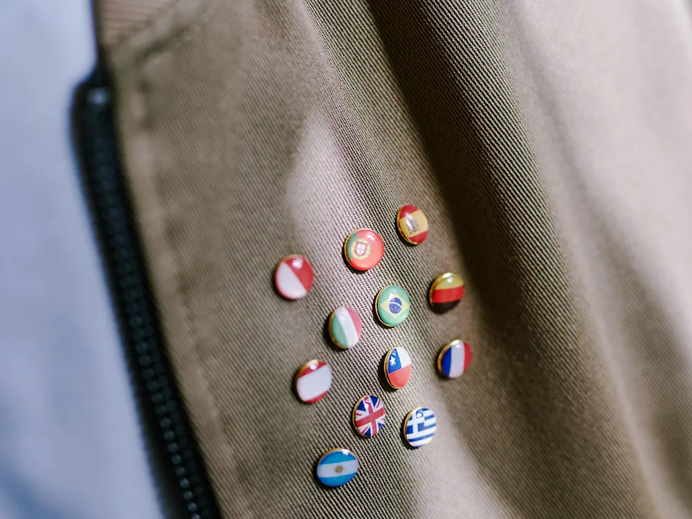 Close-up of a brown fabric with a zipper on the left and several small round pins displaying different national flags, symbolizing international diversity.