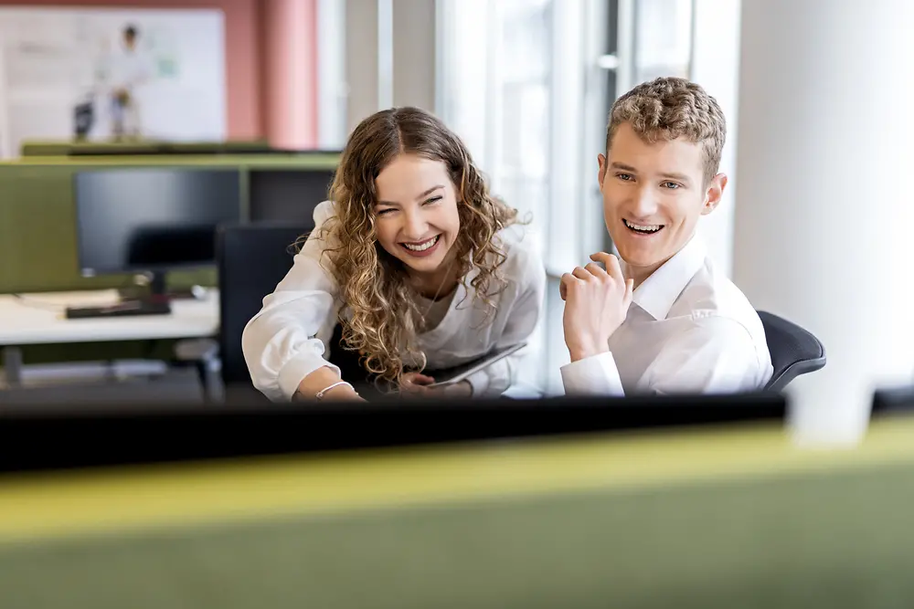 Two young professionals collaborating at a desk in a modern office environment, representing student jobs and entry-level positions.