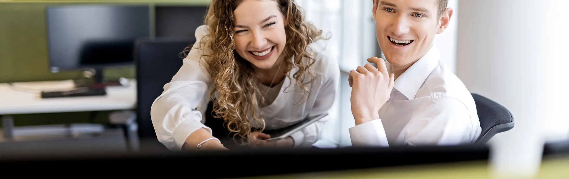 Two young professionals collaborating at a desk in a modern office environment, representing student jobs and entry-level positions.