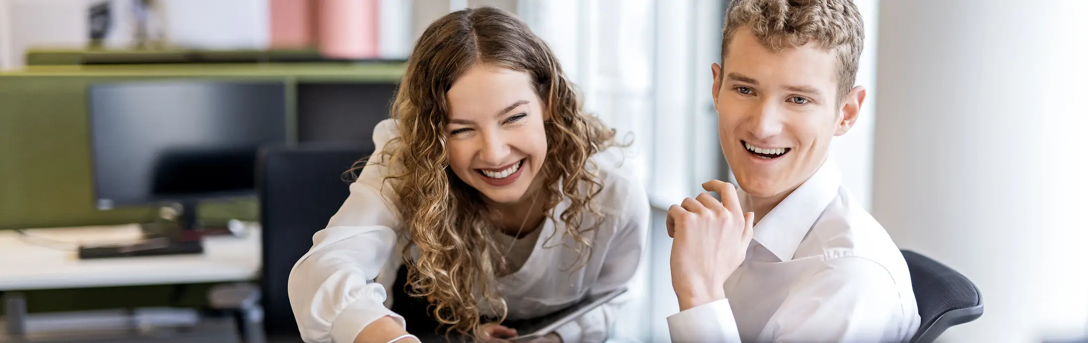 Two young professionals collaborating at a desk in a modern office environment, representing student jobs and entry-level positions.