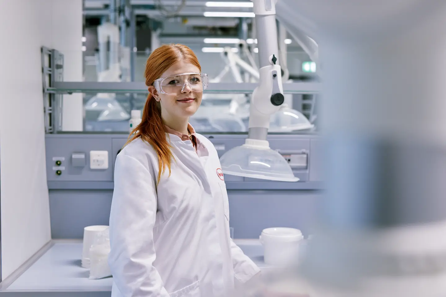 Graduate starting a career at Henkel, wearing a white lab coat and standing in a modern laboratory environment with technical equipment in the background.
