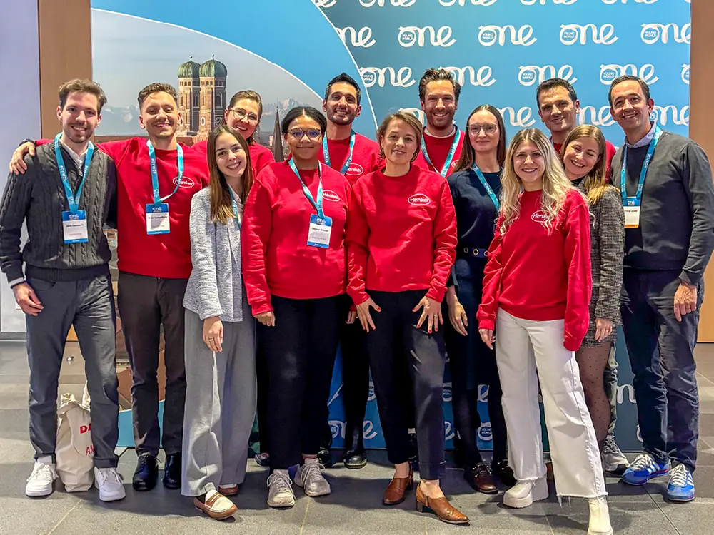 Group photo of Henkel representatives at the One Young World event in Munich, standing in front of a branded backdrop. The image highlights Henkel’s participation in the global leadership summit.