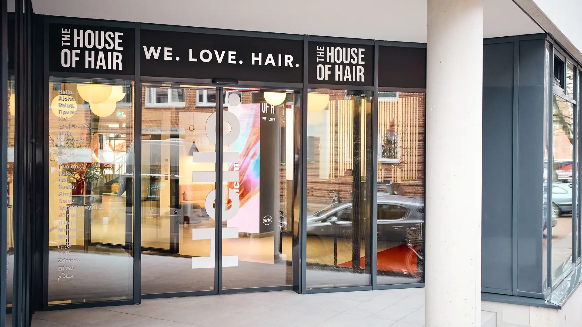 玻璃門入口。入口上方的標語為“We.Love.Hair.”左右兩側刻有文字“The House of Hair”。 