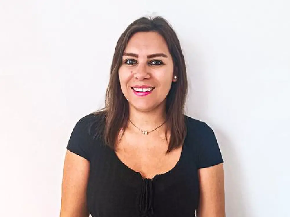
A recruitment partner standing in front of a white background, wearing a black top and beige belt, sharing tips on handling tough interview questions. 