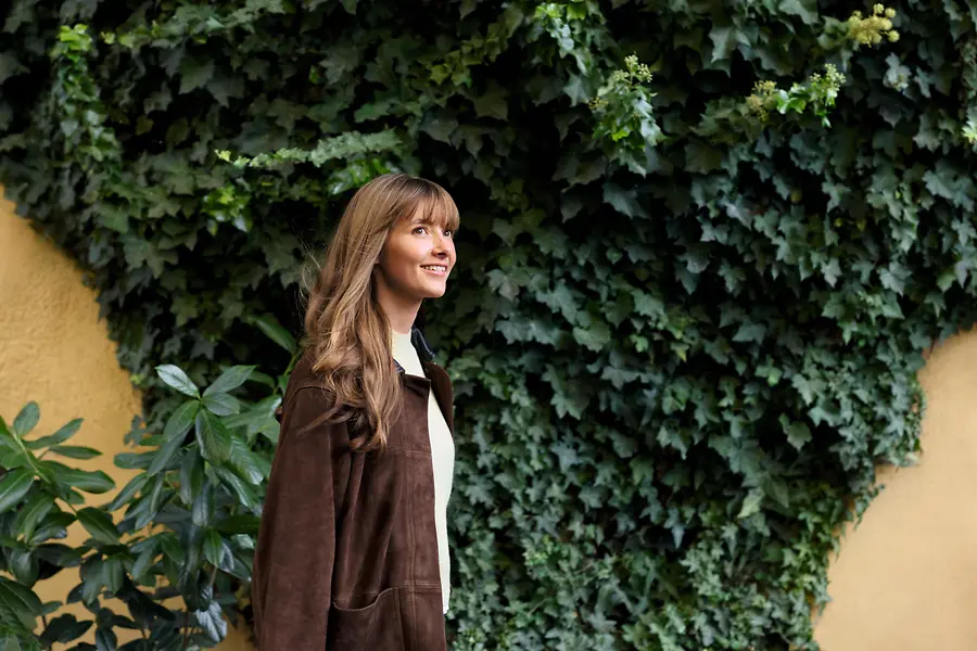 A woman walking in front of a wall covered in green plants.