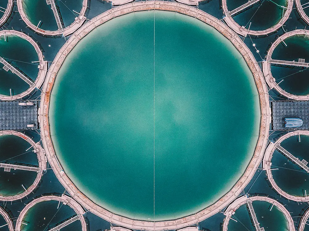 
Aerial view of large circular wastewater treatment tanks filled with turquoise water.