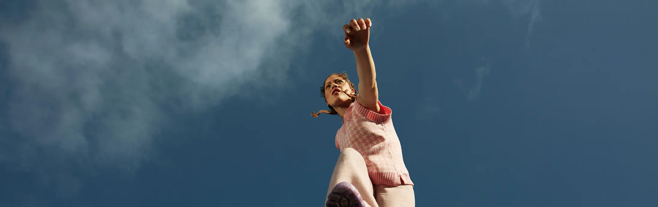 
A woman jumping enthusiastically over the camera with clear blue sky in the background