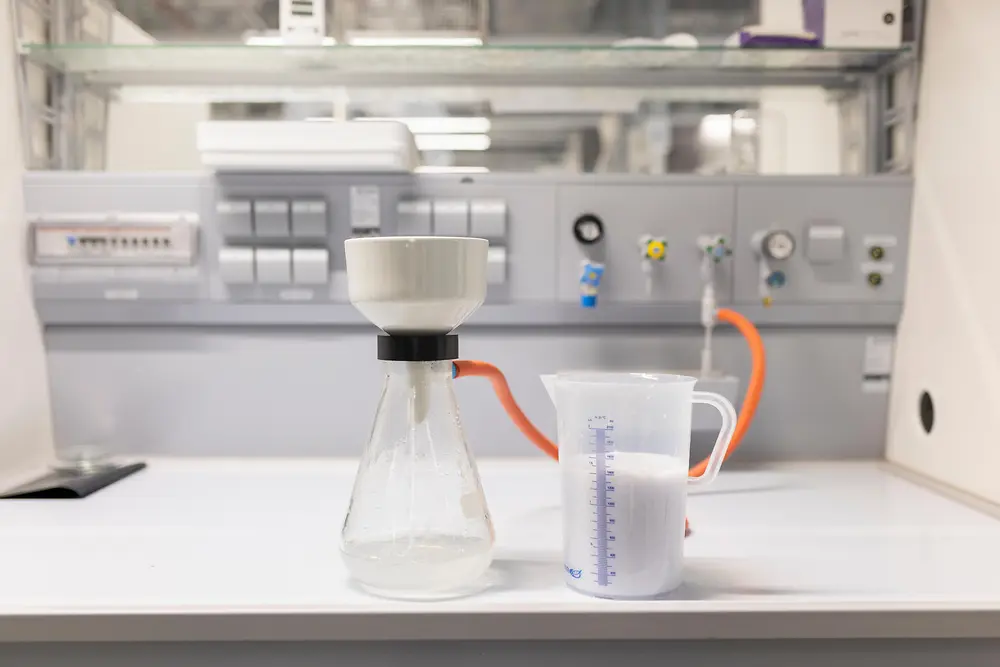 Laboratory setup with a filtration flask and funnel on the left and a beaker filled with pulp on the right, connected by an orange tube.