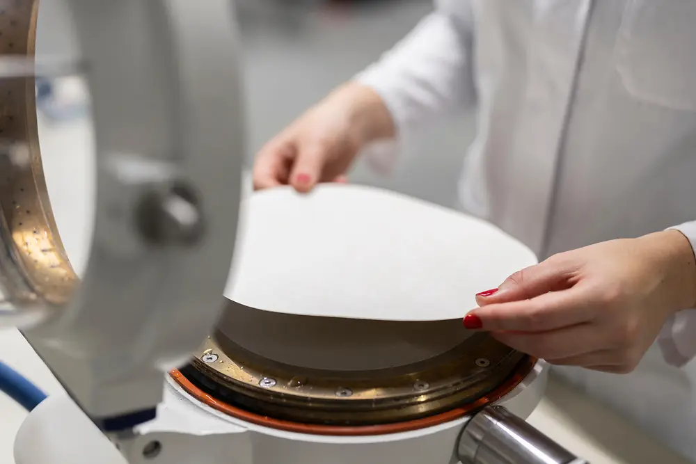 Close-up of a person in a lab coat taking a newly created paper sheet from a paper pressing and drying device.