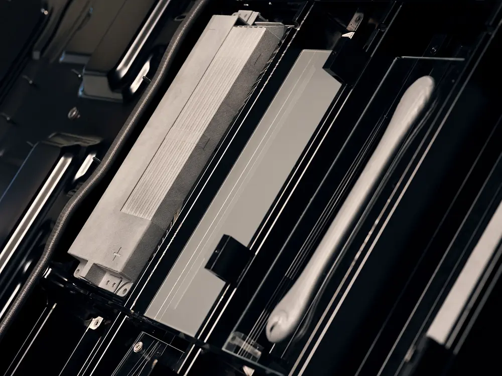 Close-up view of components inside an electric vehicle battery pack, showing metal battery cells and structural elements arranged in a compact, rectangular housing