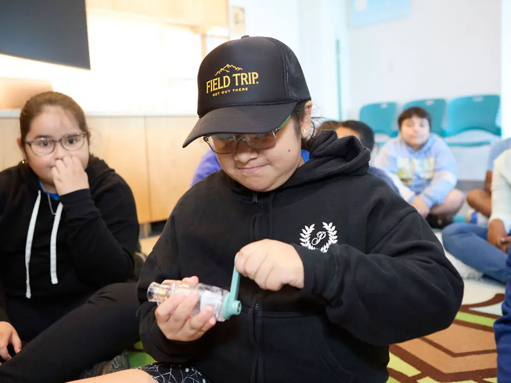 A child, surrounded by other children, is taking part in an experiment.