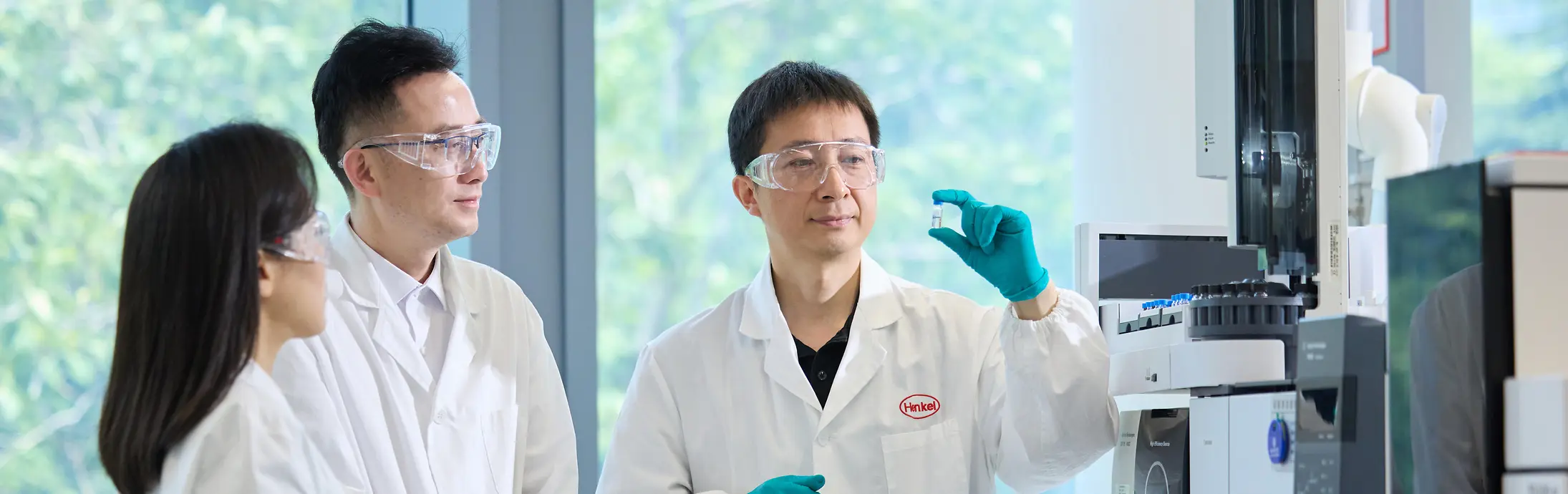 Three researchers in a laboratory examining a sample vial beside advanced analytical equipment.