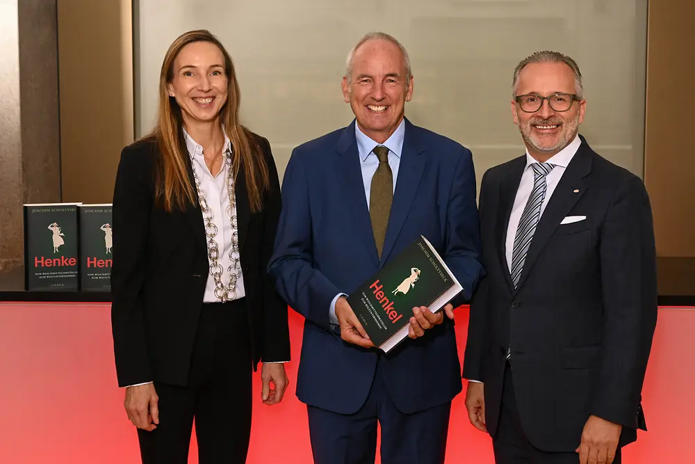 Three people at a book presentation event, with the person in the center holding a copy of a book on Henkel’s corporate history.