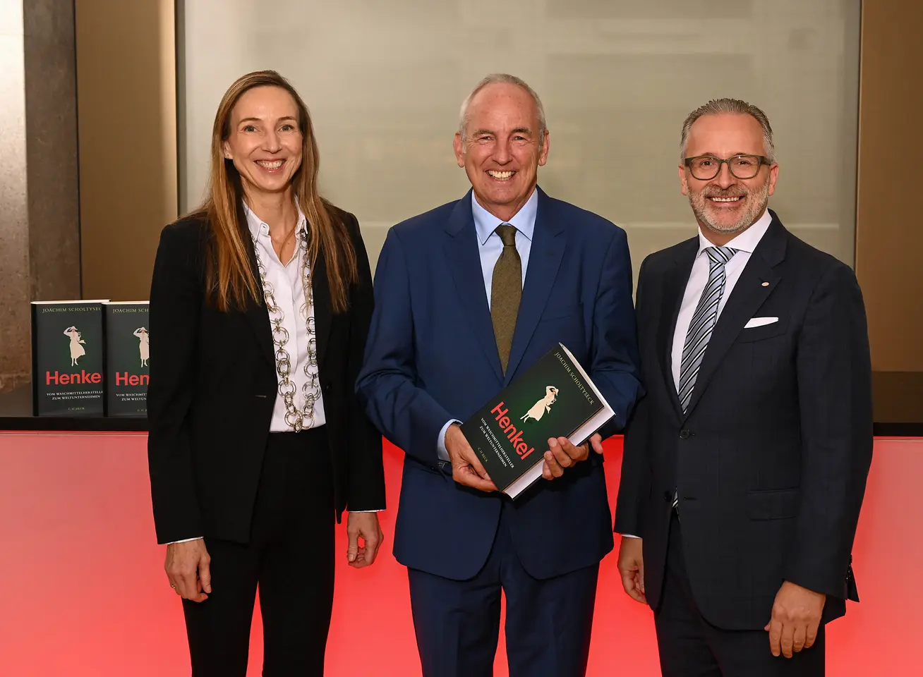 Three people at a book presentation event, with the person in the center holding a copy of a book on Henkel’s corporate history.