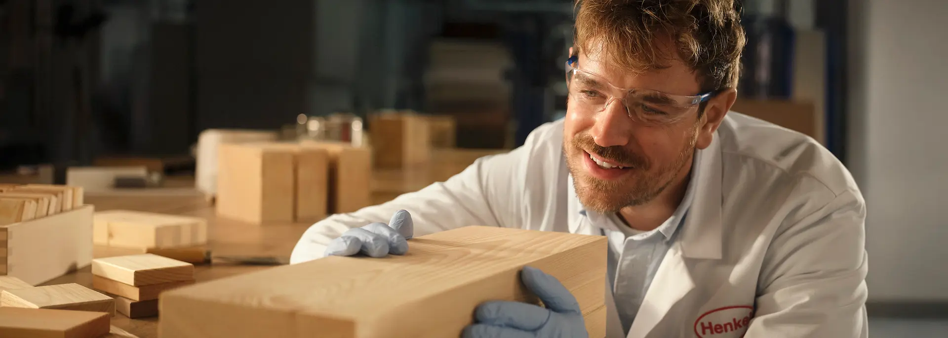 Person in a Henkel laboratory examining a rectangular wooden block on a workbench.