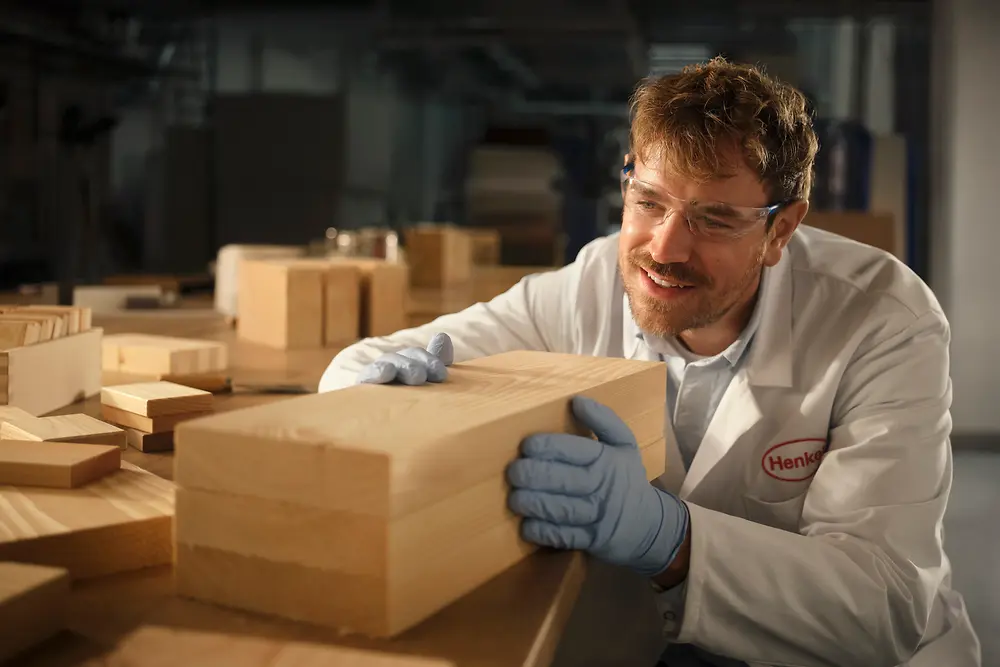 Person in a Henkel laboratory examining a rectangular wooden block on a workbench.