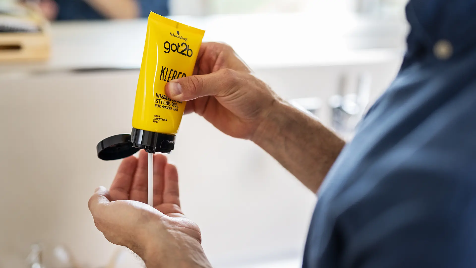 Person dispensing got2b hair product from a yellow tube into the palm of a hand.