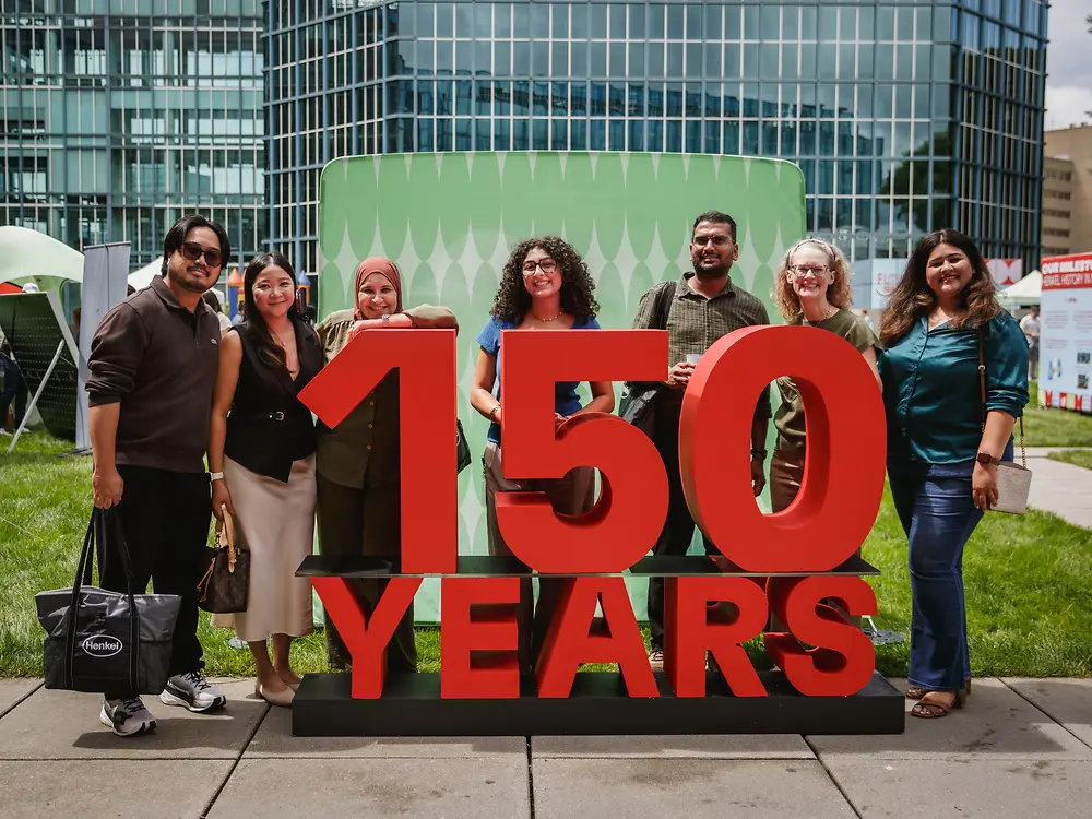 A group of employees poses in front of a large red “150 Years” anniversary installation on the festival grounds.