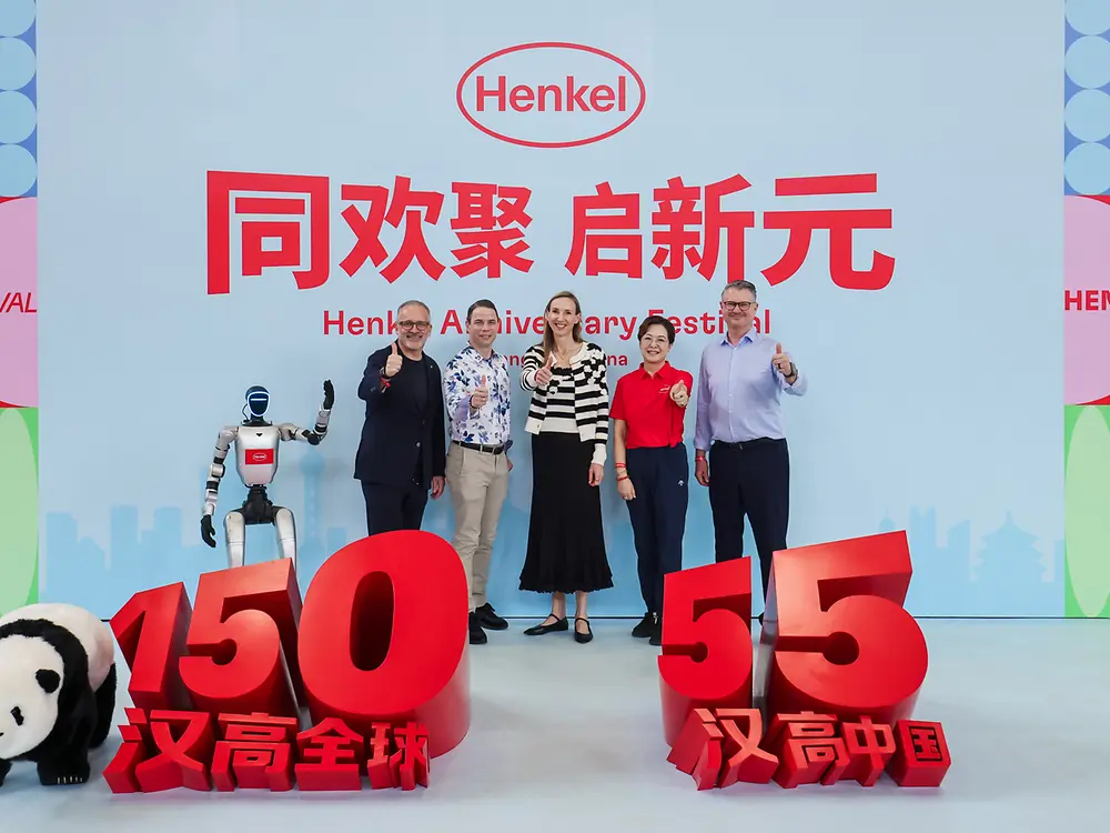 Five people gathered in front of a stage backdrop featuring anniversary branding and a large red 