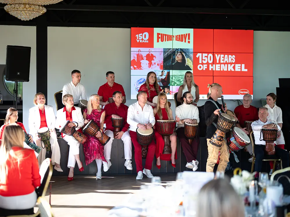 People take part in a ceremony on stage in front of a large screen displaying Henkel’s 150th anniversary branding.