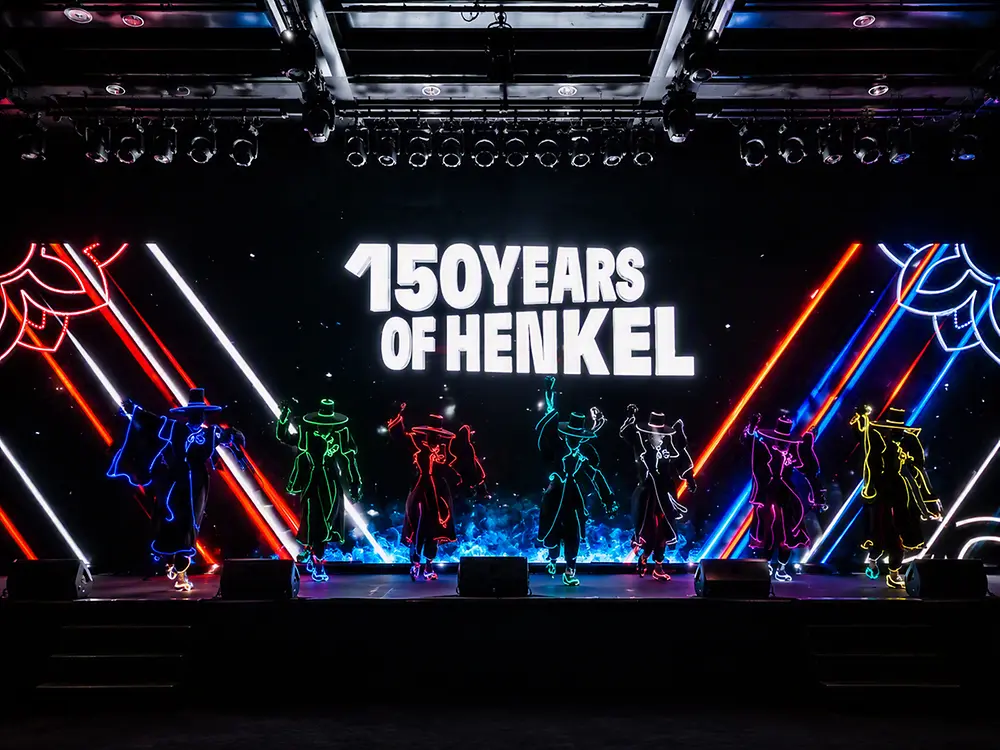 Performers take part in a stage show in front of a large “150 Years of Henkel” anniversary display.