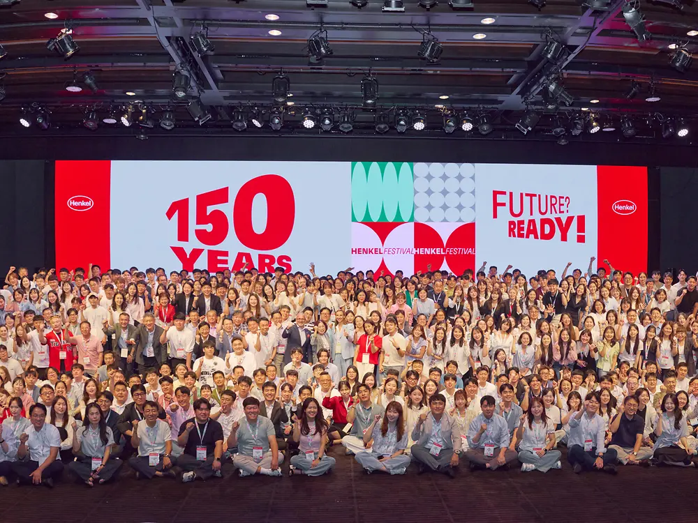 Employees gather on stage and in front of a large anniversary backdrop during Henkel Korea’s 150th anniversary celebration.