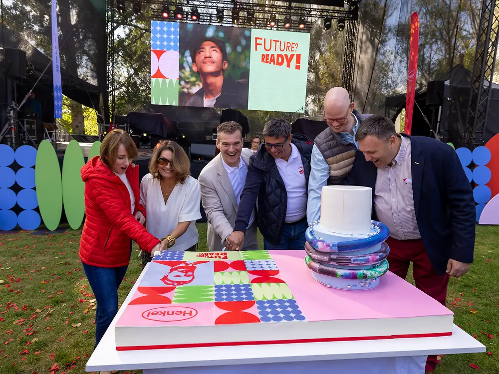 Group of people standing around a large anniversary cake during a celebration event.