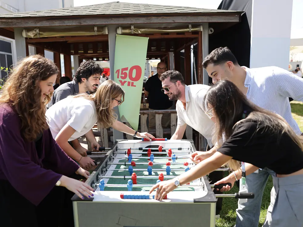 Employees gather around a table football game during a Henkel anniversary event in Türkiye.