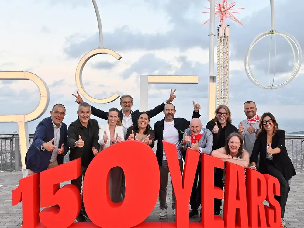 Group poses on a terrace behind large red “150 Years” letters.