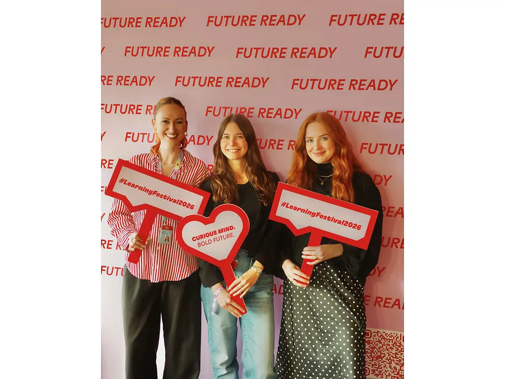 Three people holding red speech-bubble and heart-shaped signs in front of a “Future Ready” backdrop.arge red “150 Years” letters.