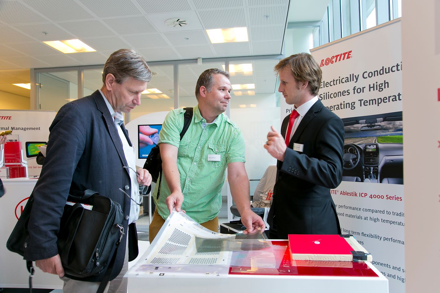 
Electronics expert Nicholas Havemann (right) explains the advantages of electrically conductive adhesives for temperature sensitive components in vehicles to two interested customers. 