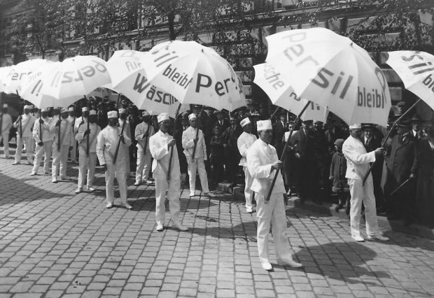 Men dressed in white and holding gigantic Persil sun umbrellas 