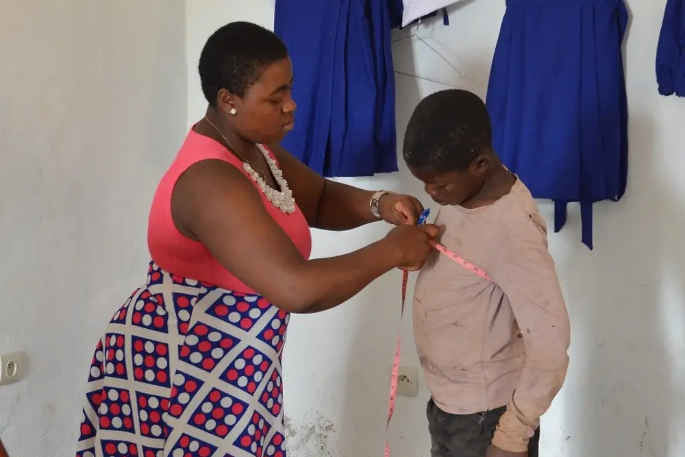 The seamstress takes the measurements for a new school uniform,