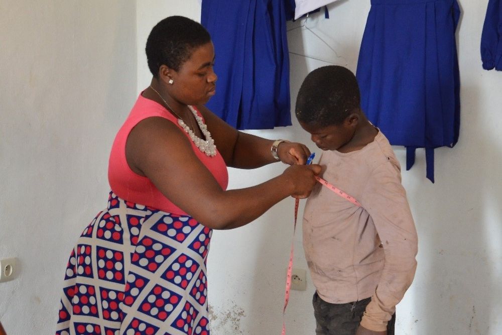 The seamstress takes the measurements for a new school uniform,