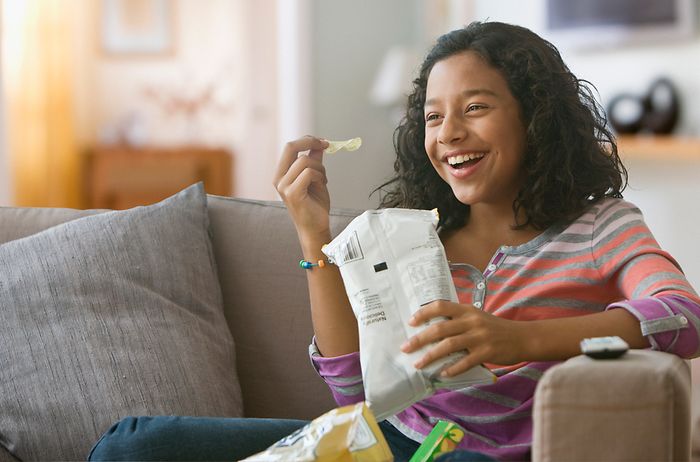 A laughing girl eating potato chips out of a bag