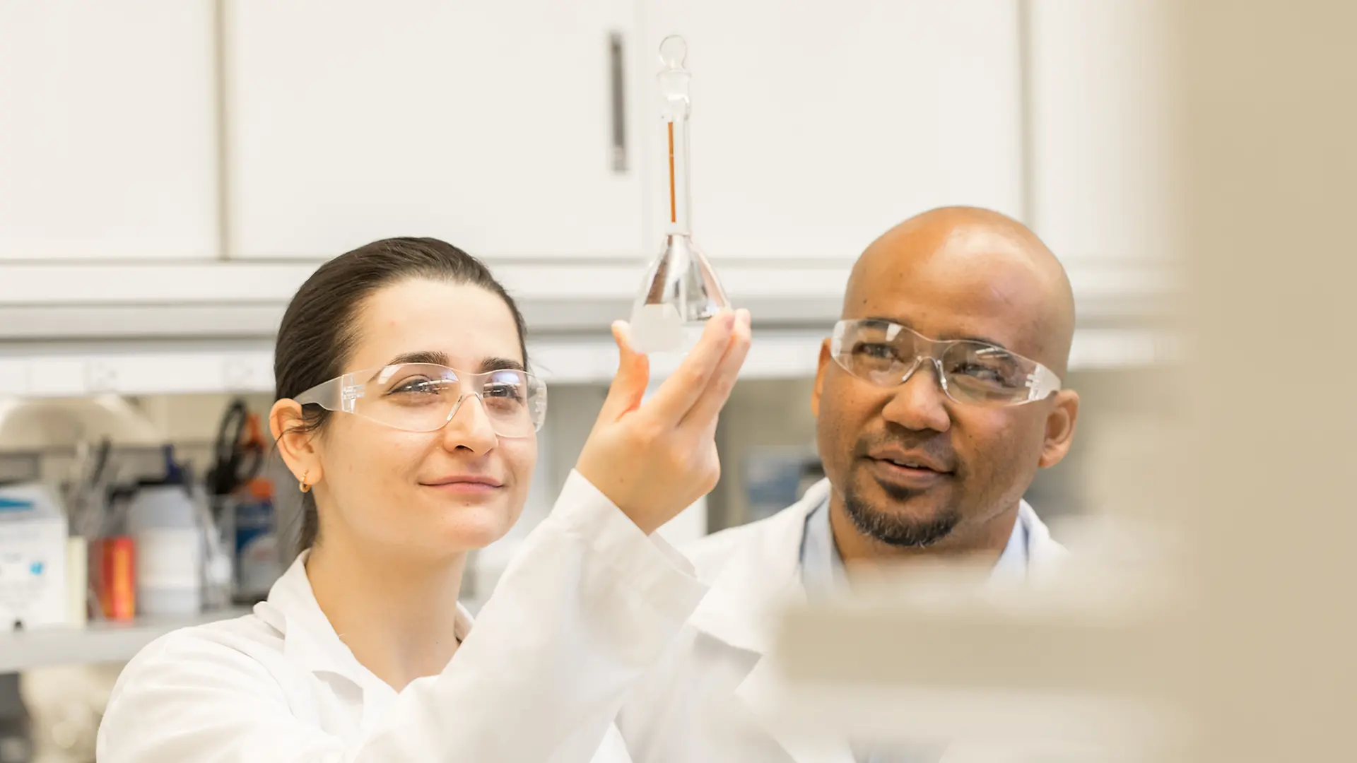 A female and a male lab worker contemplate a liquid in a vial