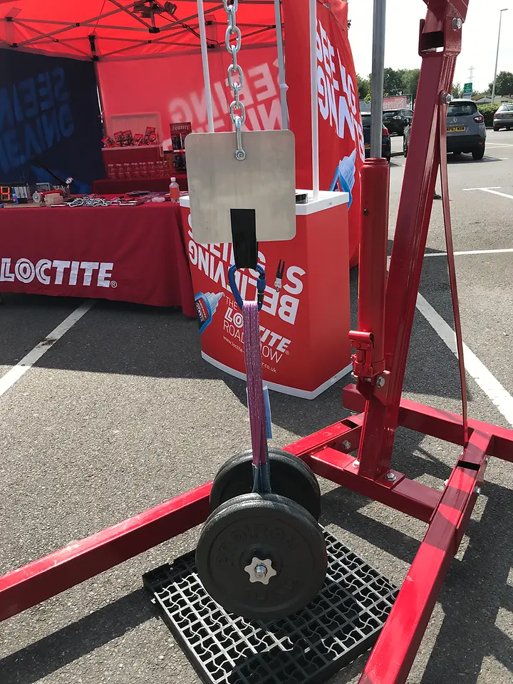 A large dumbbell hanging from a metal plate, fastened with a black Loctite tape